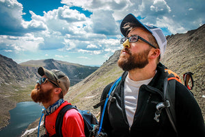 Two men on a mountain overlooking a lake with Nöz reef safe sunscreen on their noses